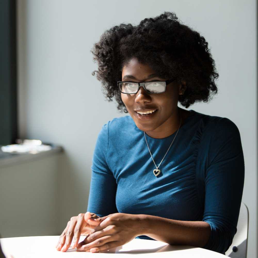 Smiling woman wearing blue shirt sitting beside table.